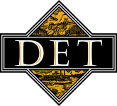 Elegant emblem with the letters "det" displayed in a bold font, set against a black and gold diamond-shaped background with intricate designs.