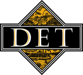 Elegant emblem with the letters "det" displayed in a bold font, set against a black and gold diamond-shaped background with intricate designs.