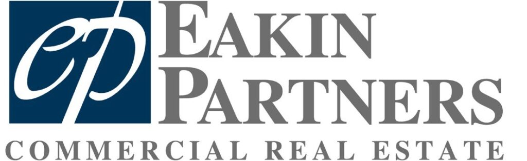 The image depicts a logo for "eakin partners" featuring a stylized letter "e" resembling a pair of buildings or architectural elements within an oval shape, alongside the text "eakin estate" and "commercial real estate" indicating their industry focus. the logo utilizes a color scheme of blue and white.