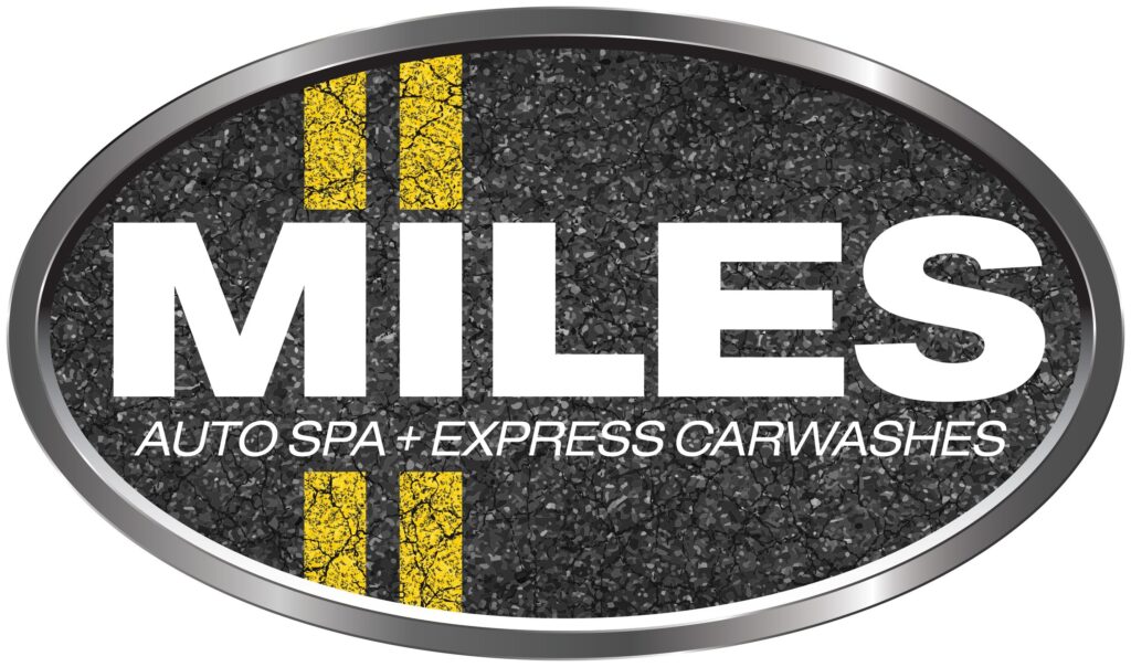 Oval sign with a simulated asphalt texture and double yellow lines, featuring the word "miles" in large white letters, followed by "auto spa + express carwashes" in smaller text, against a grey and black oval border.