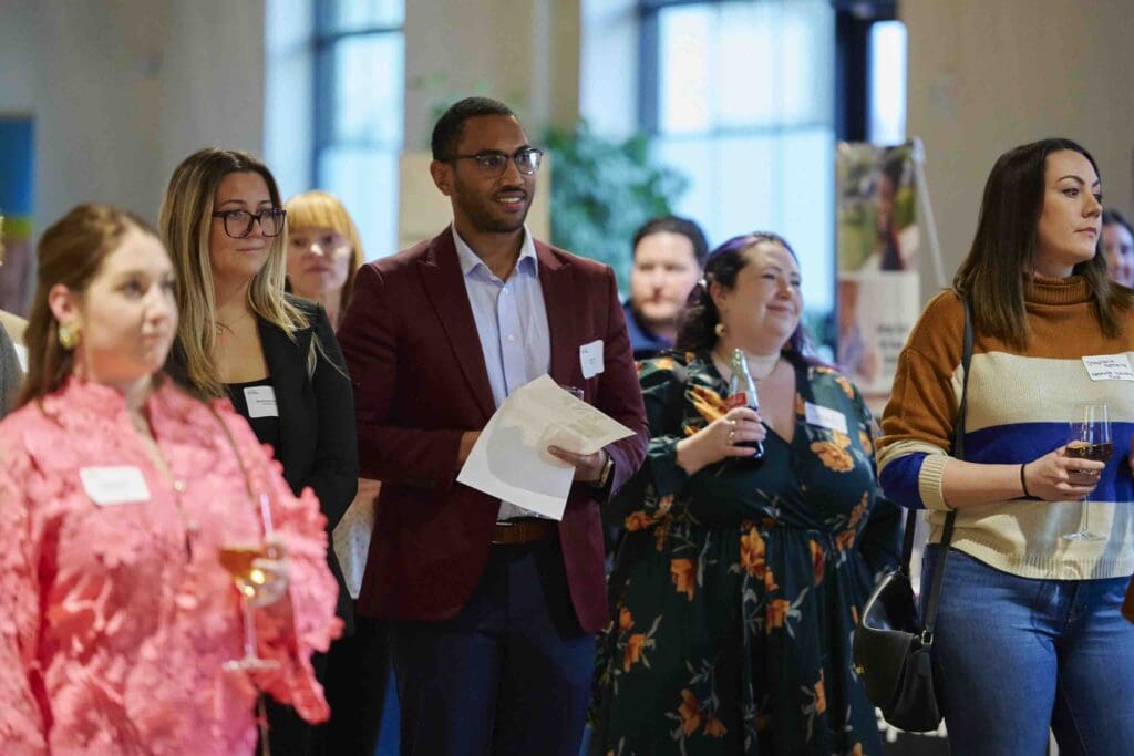 A group of attentive professionals with name tags at a networking event or conference, participating in a session or listening to a presentation.