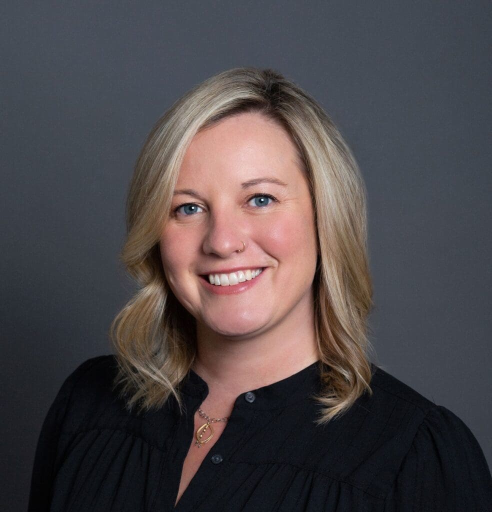 Professional woman smiling confidently for a corporate headshot against a grey backdrop.