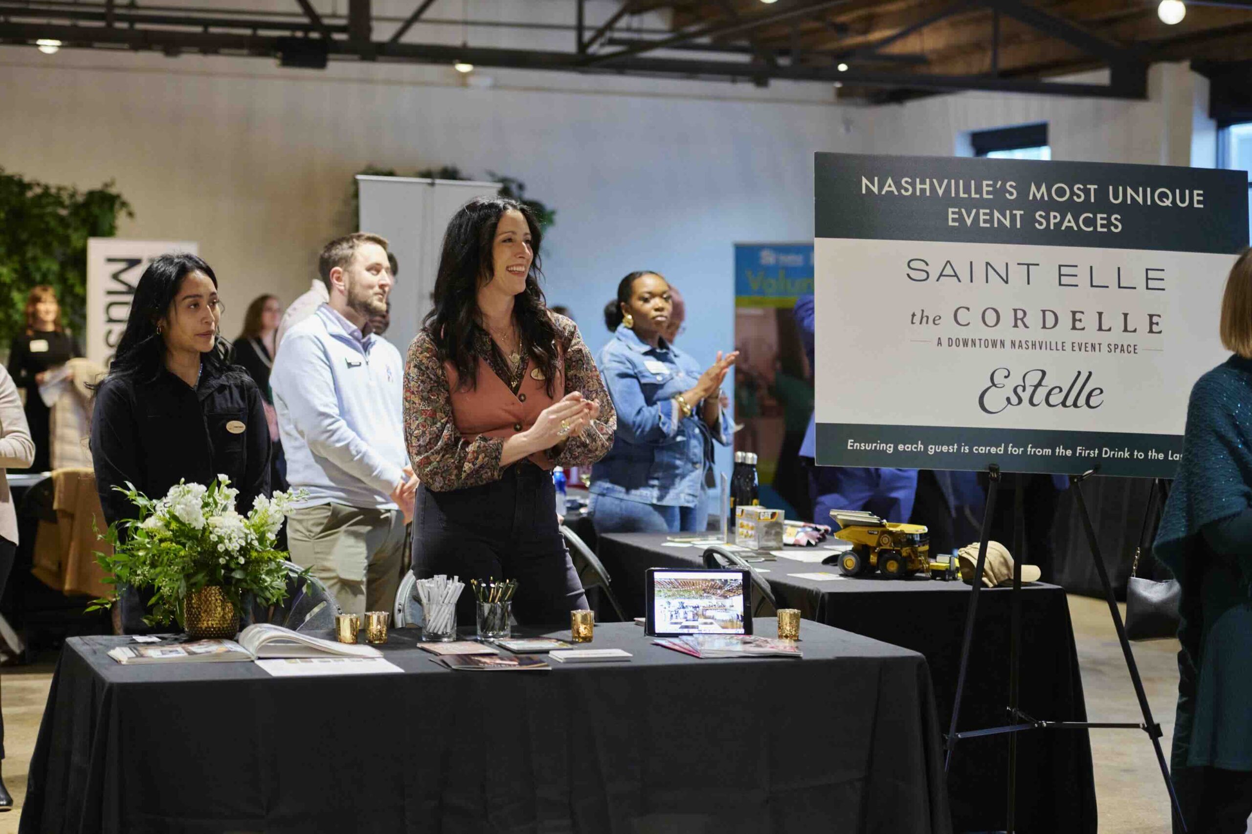 Group of people at an event showcasing "nashville's most unique event spaces," with a focus on saint elle & estelle. attendees are interacting and exploring the venue offerings, with promotional materials displayed on the tables.